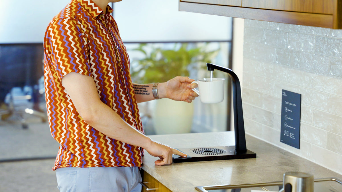A person filling a mug from a Borg & Overström dispenser in an office kitchen