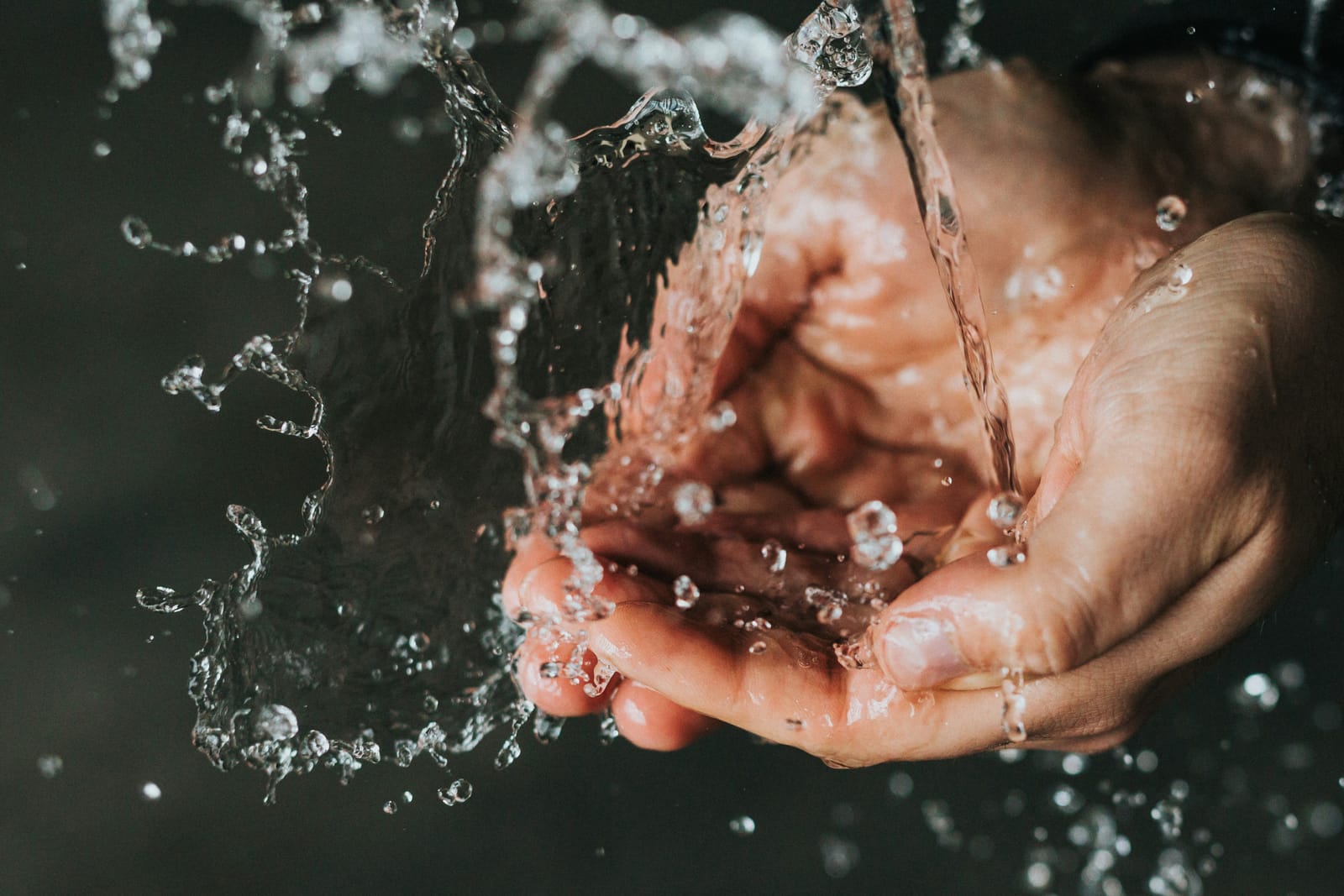Hands catching splashing water against a dark background