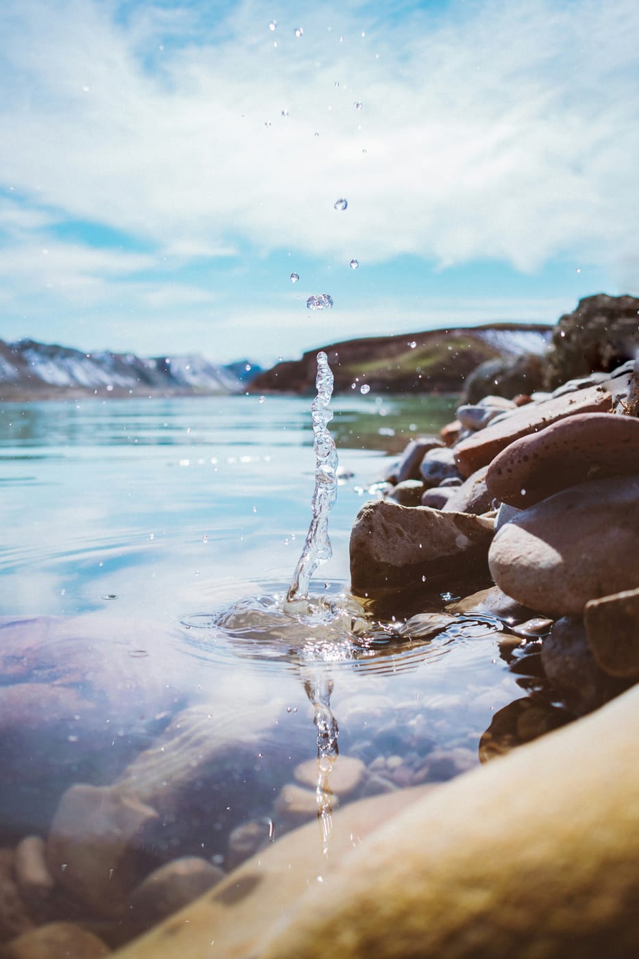 Clear spring water bubbling up among lakeside rocks, mountains in the background