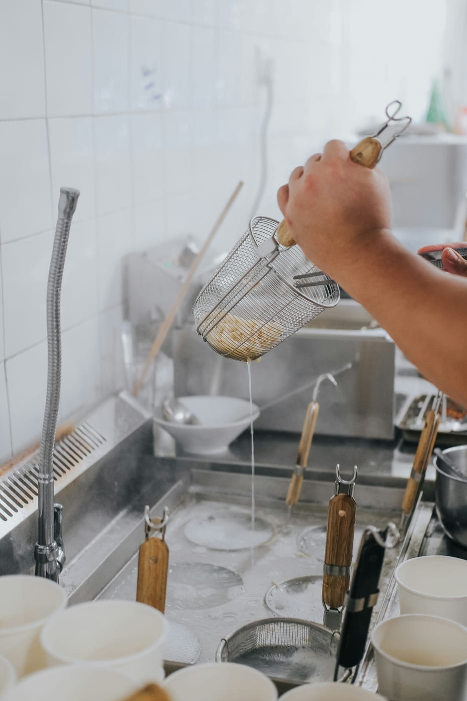 Restaurant kitchen staff rinsing a fry basket at a commercial sink