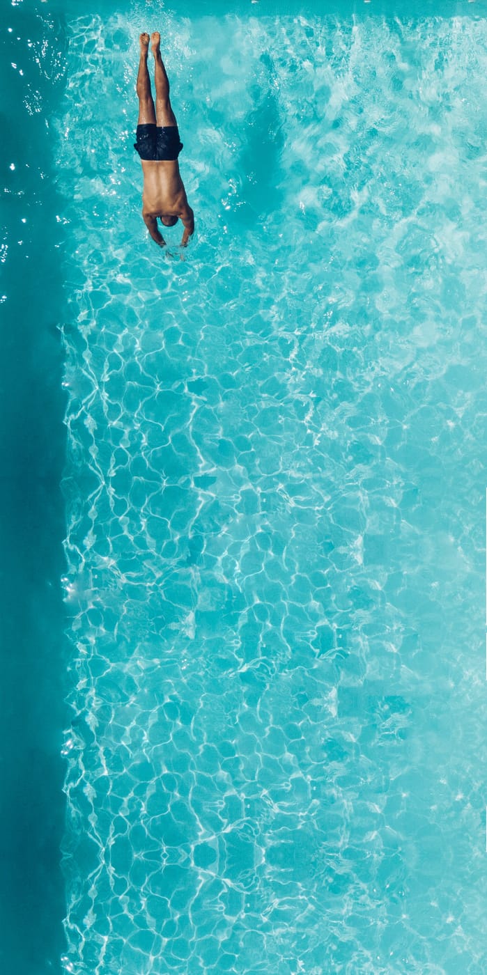 Swimmer diving into a clear turquoise hotel pool, aerial view